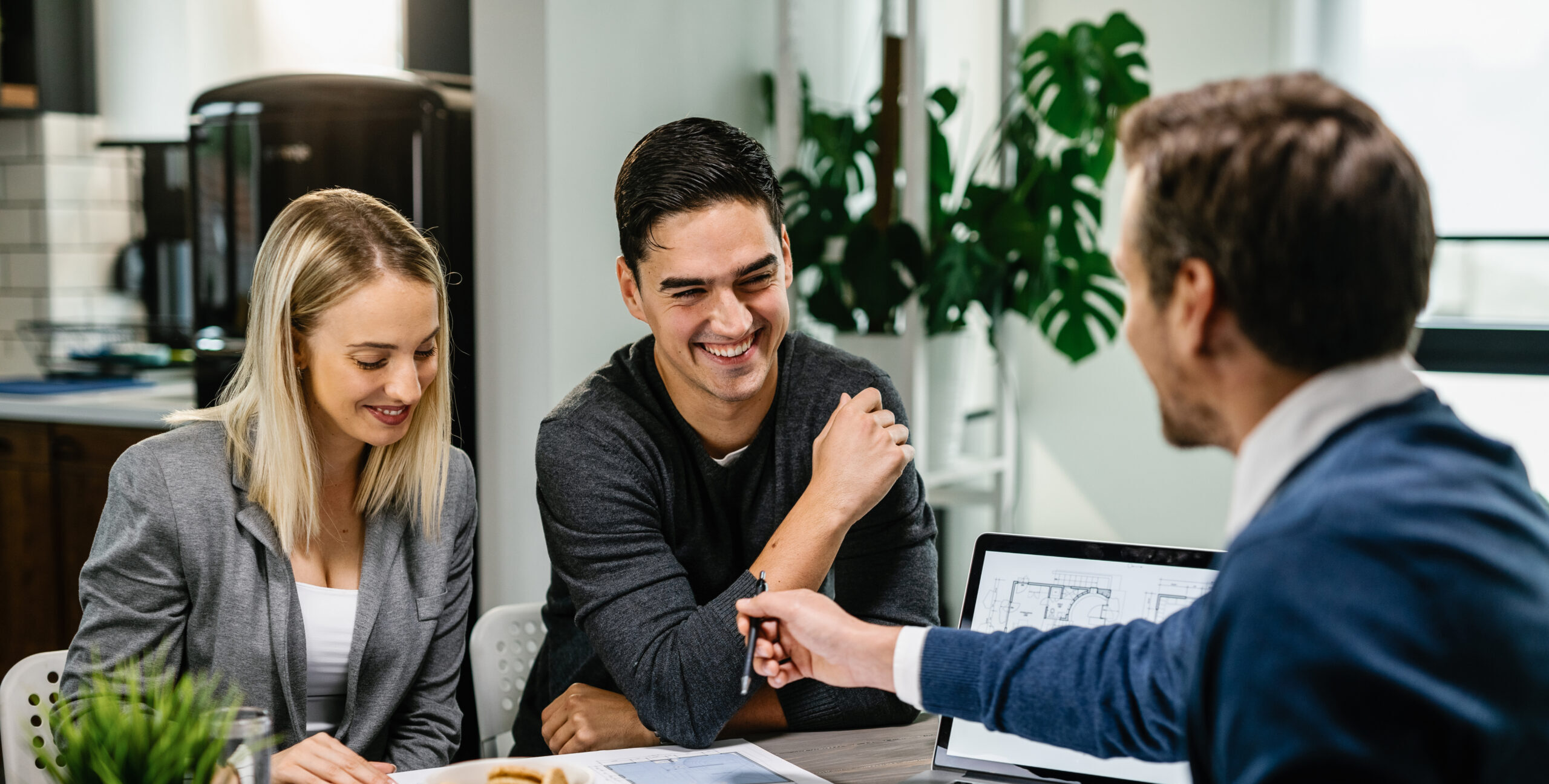 Happy couple having a meeting with real estate agent and analyzing blueprints while communicating.